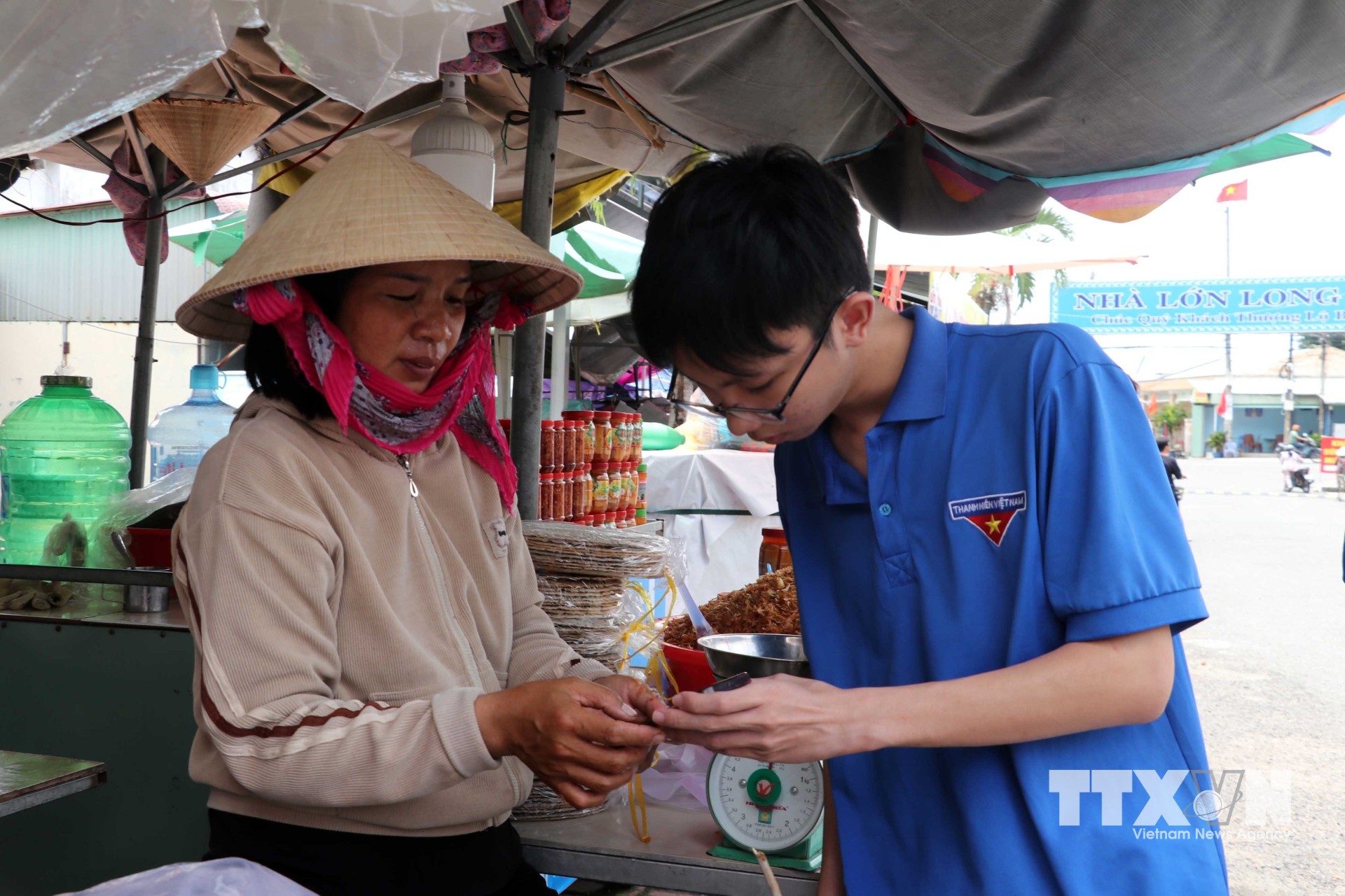 Tổ công nghệ số Đoàn Thanh niên xã Long Sơn cài đặt và hướng dẫn tiểu thương tại khu vực bán hàng hải sản phía trước Nhà lớn Long Sơn. (Ảnh: Đoàn Mạnh Dương/TTXVN)